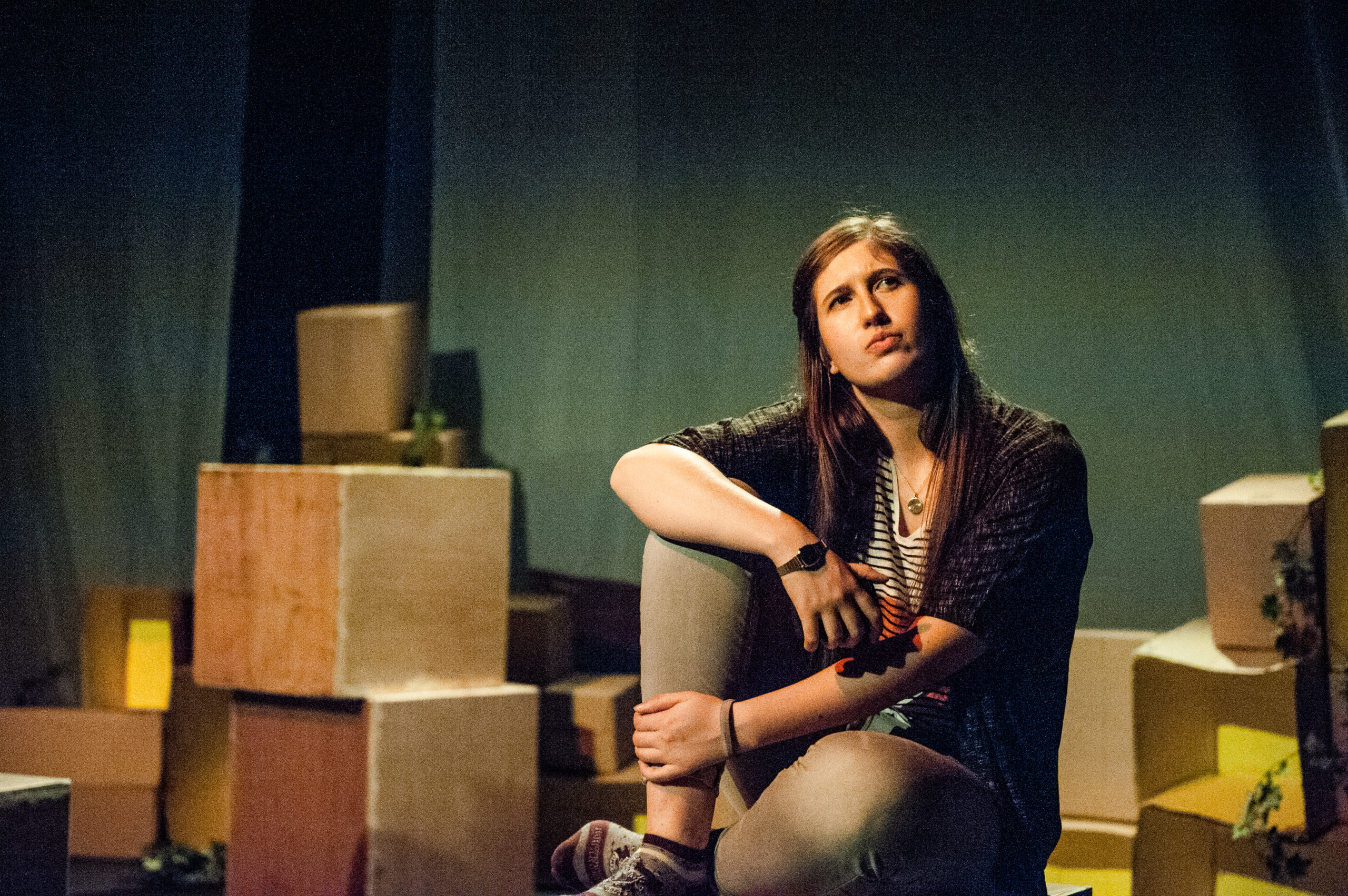 A young woman sits clutching her knees with a thoughtful expression on her face.