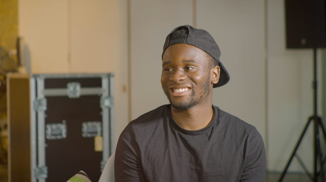 Thumbnail image for the 'Case study film: Sonny Nwachukwu' video. Sonny is smiling at the camera, wearing a black t-shirt, and a black backwards baseball cap.
