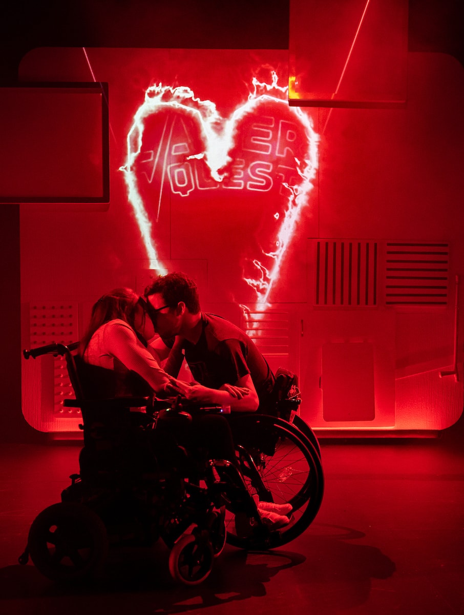Maya Coates and Jack Hunter are locked in a passionate kiss, whilst cast in red light.