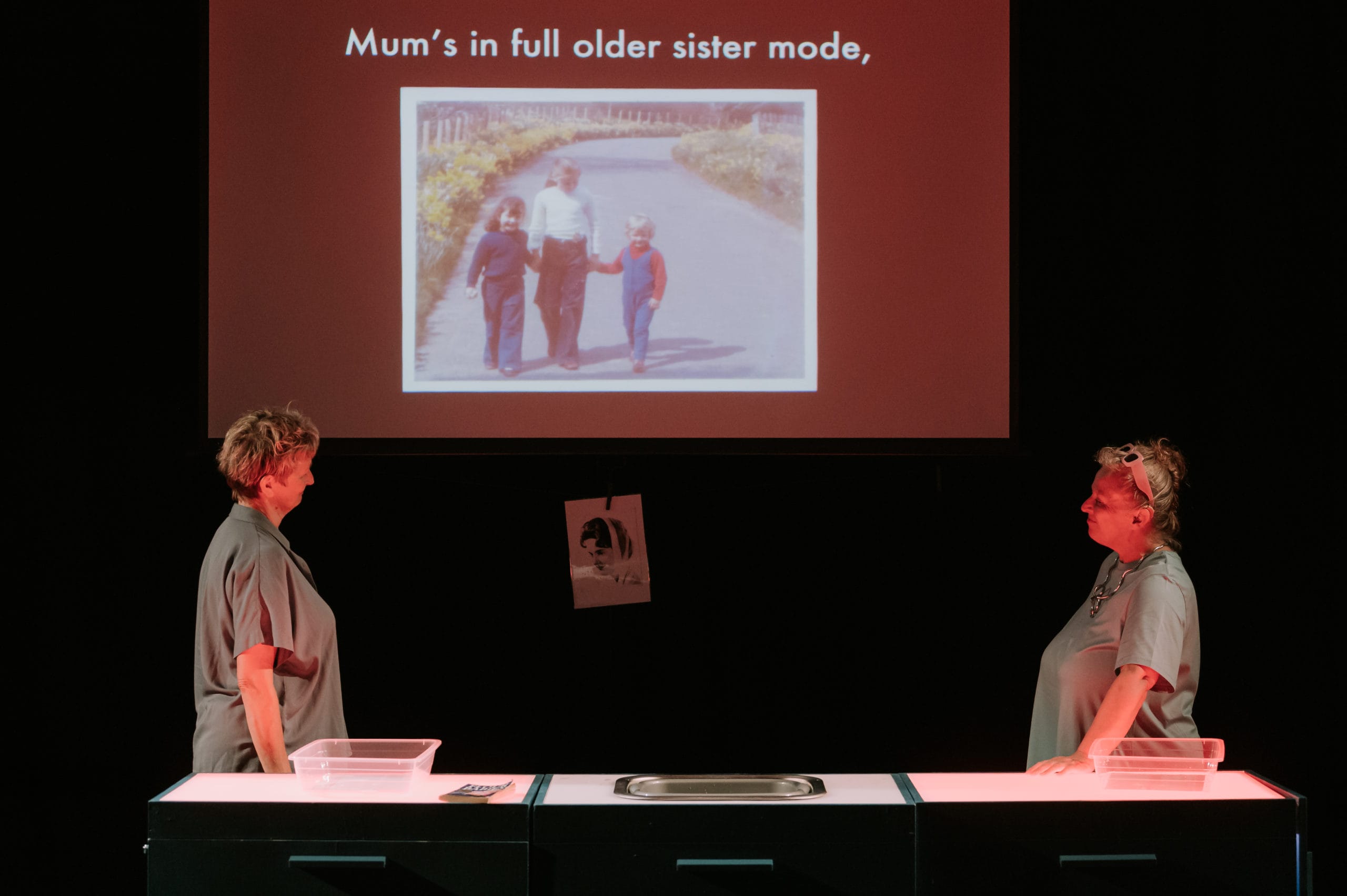 Two women stand facing each other, a screen with a picture is projected in the background.