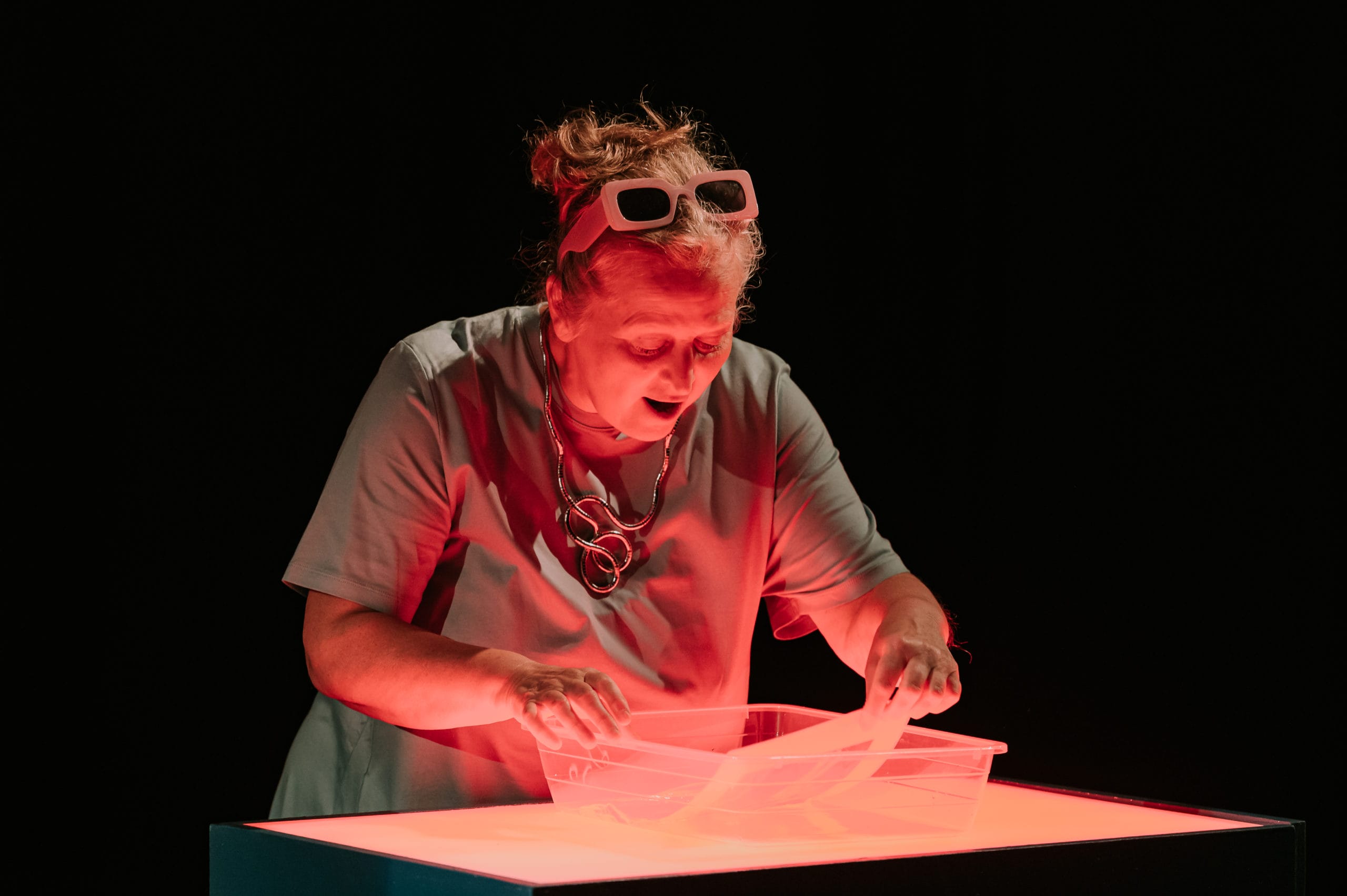 A white woman stands developing a photo in developing liquid, cast in red light.