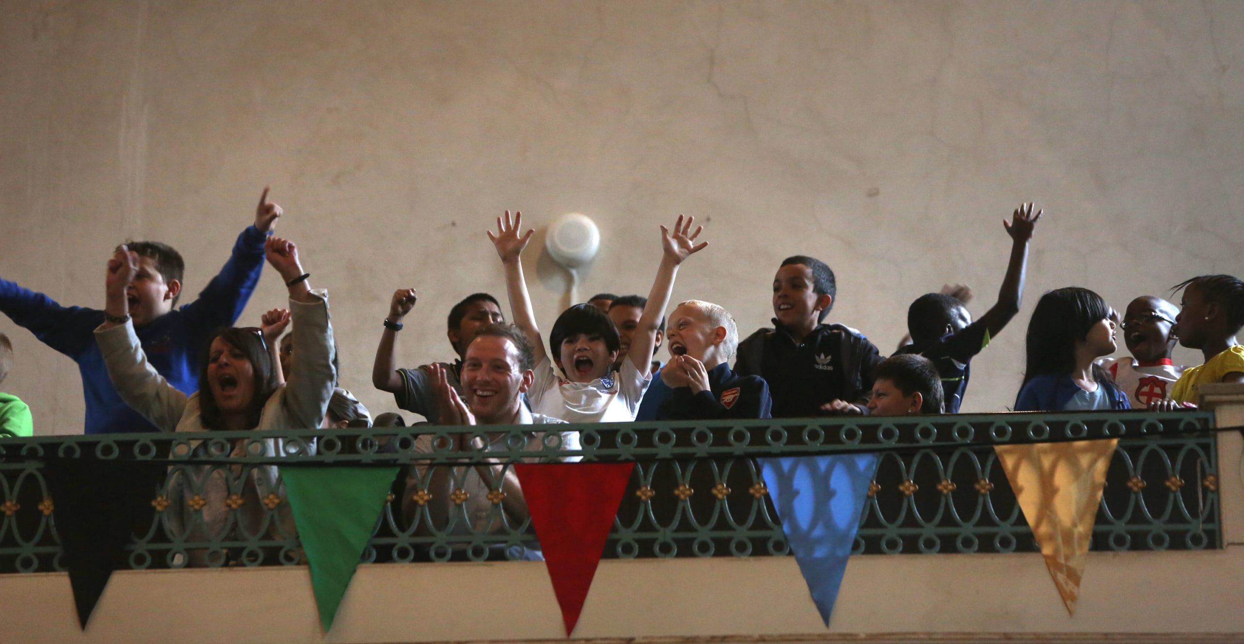 A group of young people on a balcony. They have their arms in the air and are cheering.