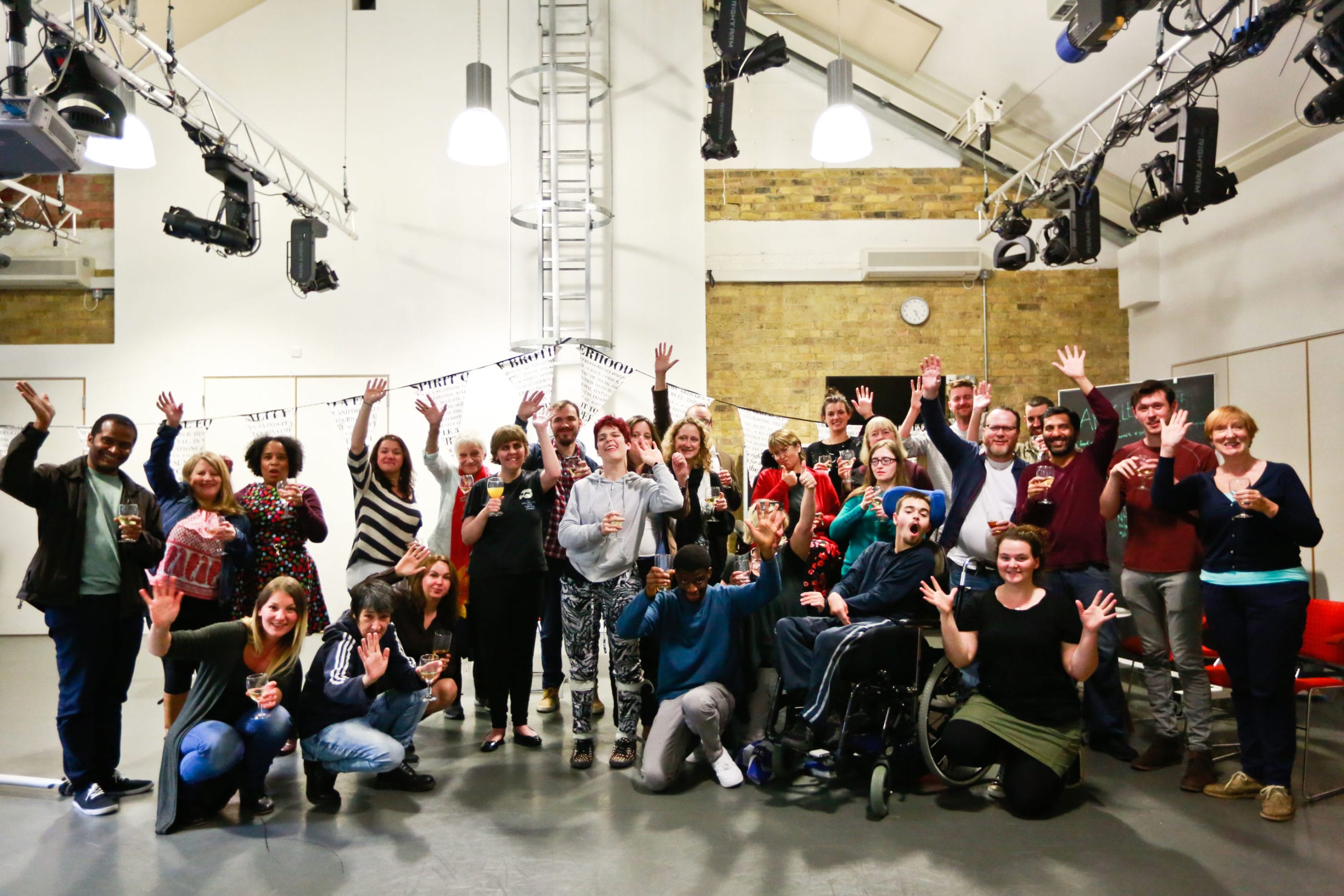 A large crowd of people, all stood together cheering and toasting drinks.