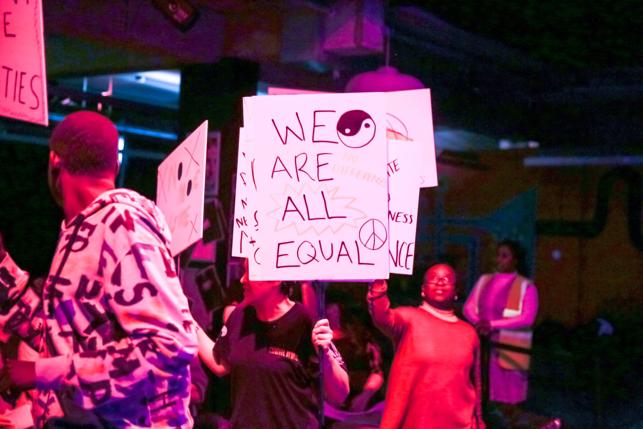 A group of protesters holding picket signs. The one at the front reads We Are All Equal.