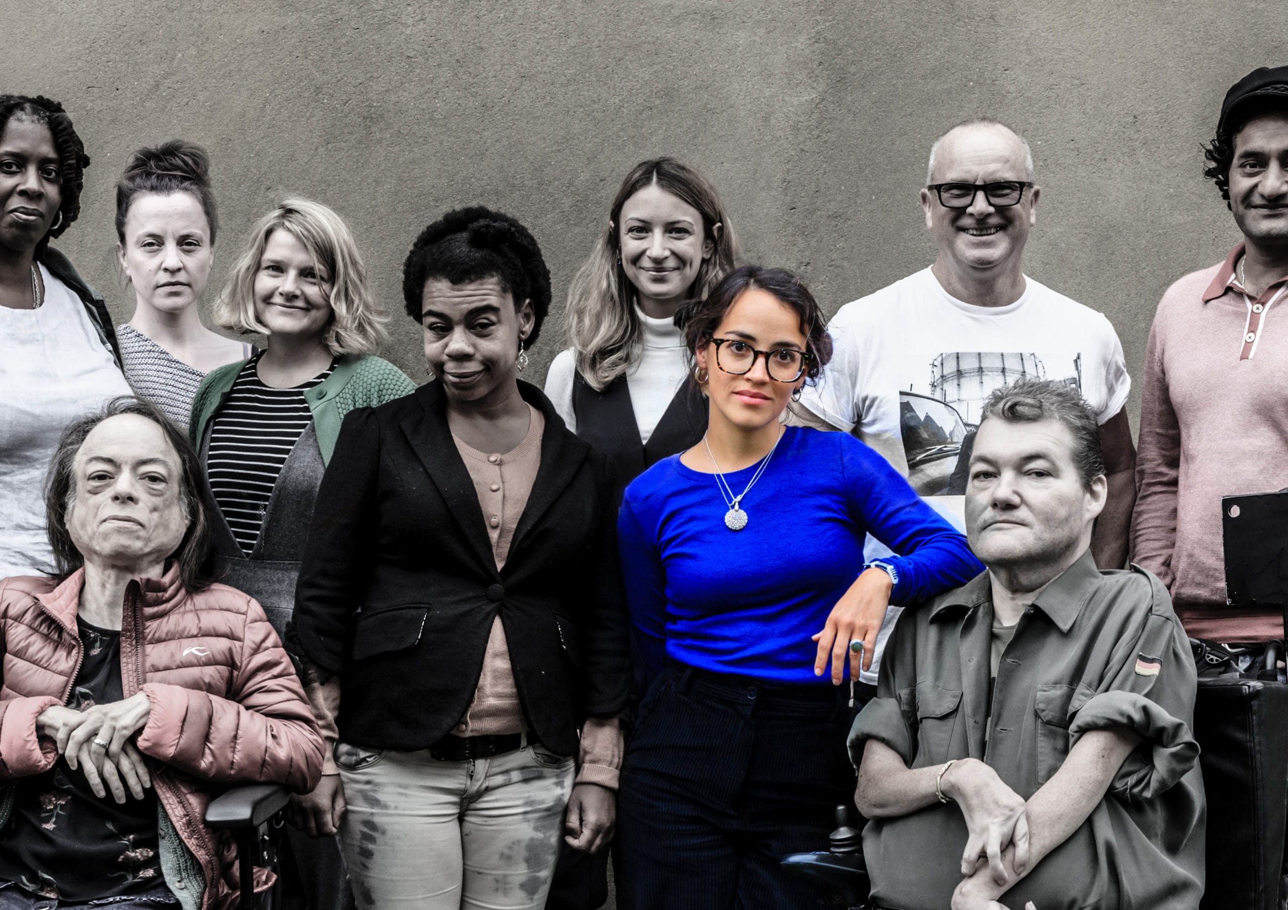 A large group of people all staring directly at the camera. The colours are muted, only picking out hints of bold primary colours in the peoples clothes