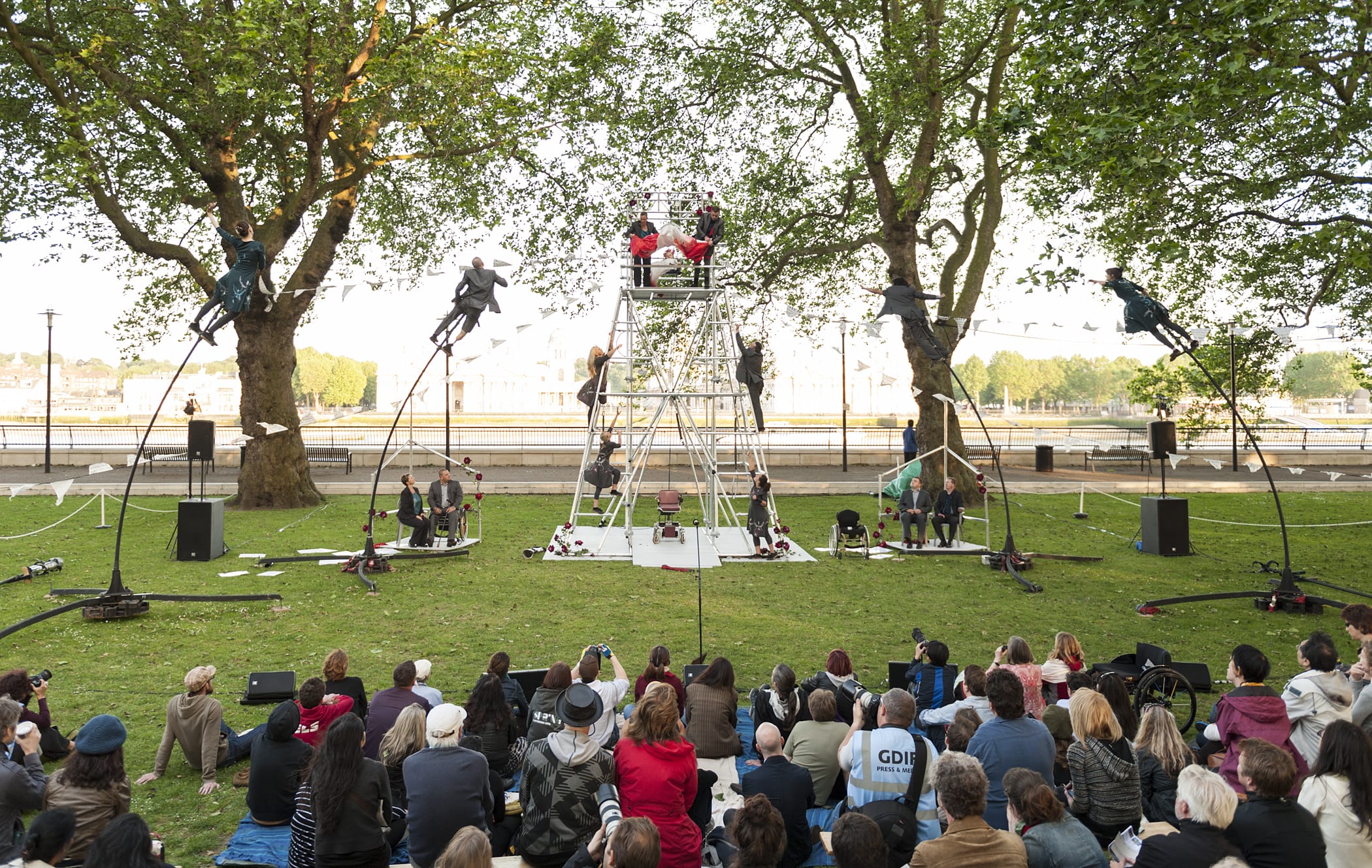 A group of actors stand gathered around a large metal scaffolding structure.