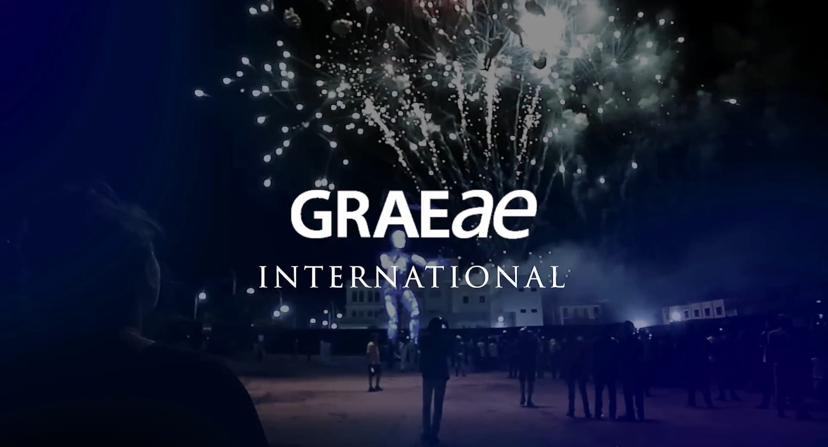 A photograph of fire works and a huge marionette puppet being operated through a crowd of people, provides the backdrop for white text that reads "Graeae International".