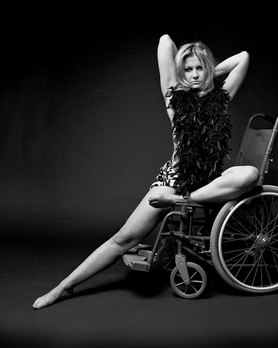 A white woman strikes a dramatic pose whilst sitting on a wheelchair.