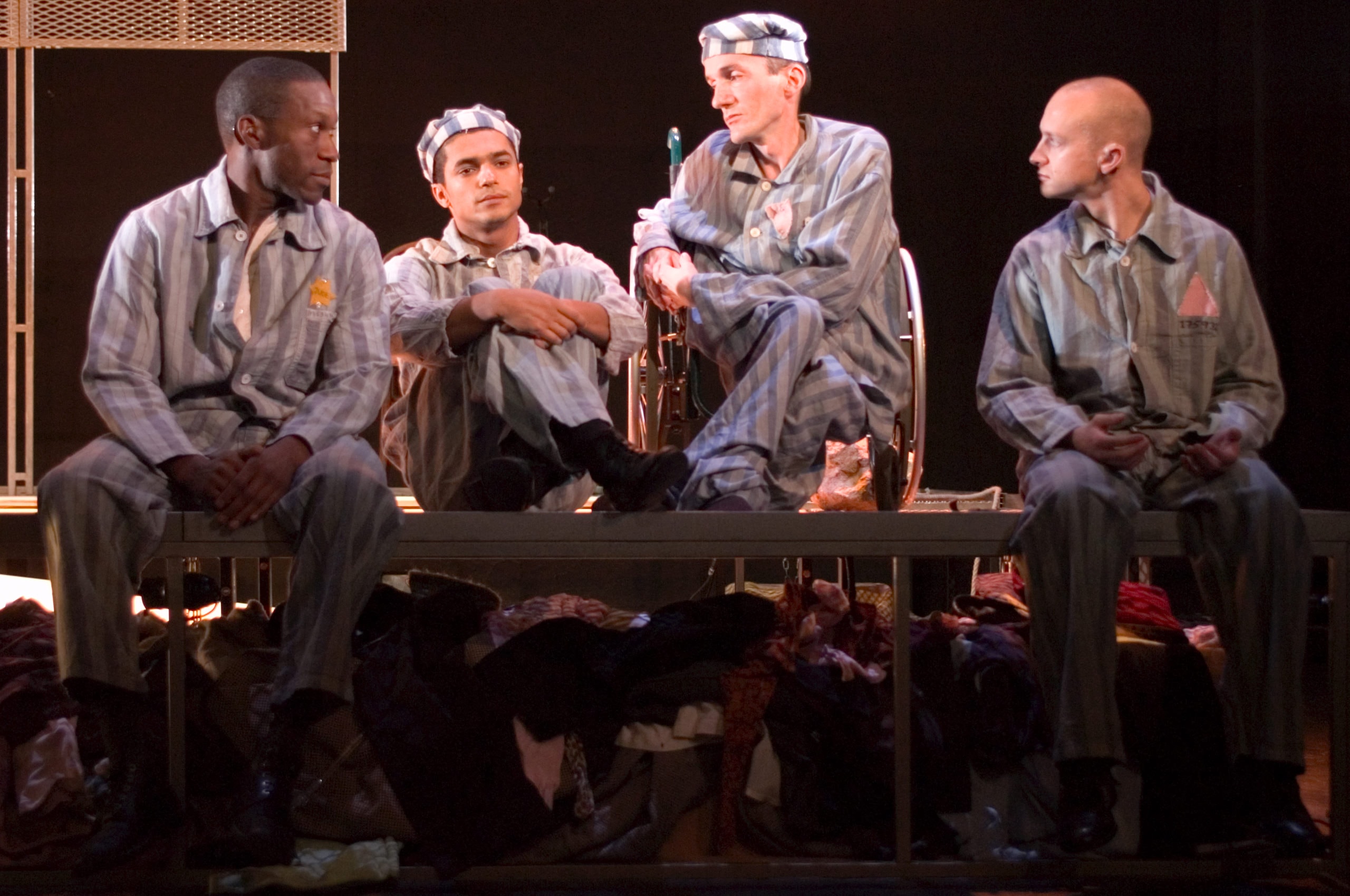 four performers sit on stage, they are all in the uniforms of people in concentration camps. They look despairingly at each other