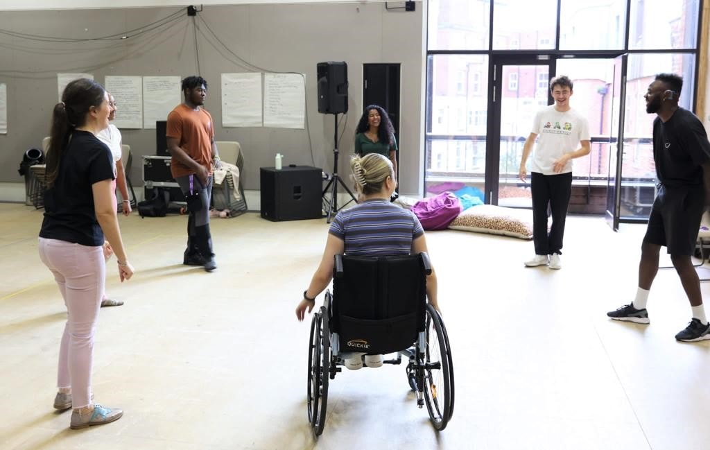 A group of actors make a circle in a rehearsals space