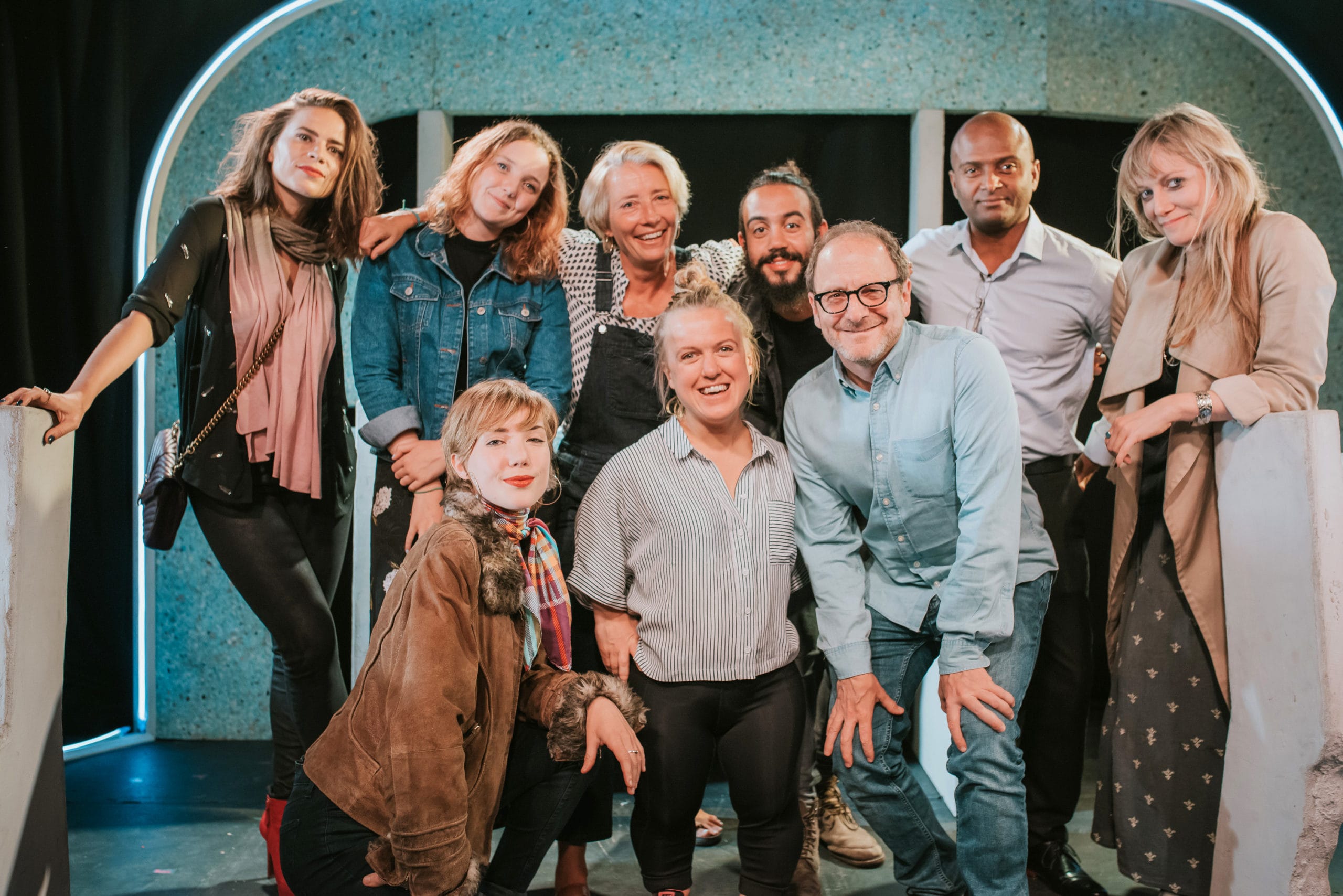 The cast of the Graeae Production of Cosmic Scallies, gathered around Graeae Patron, Emma Thompson for a group picture. Some people are crouching in front. They are all smiling at the camera.