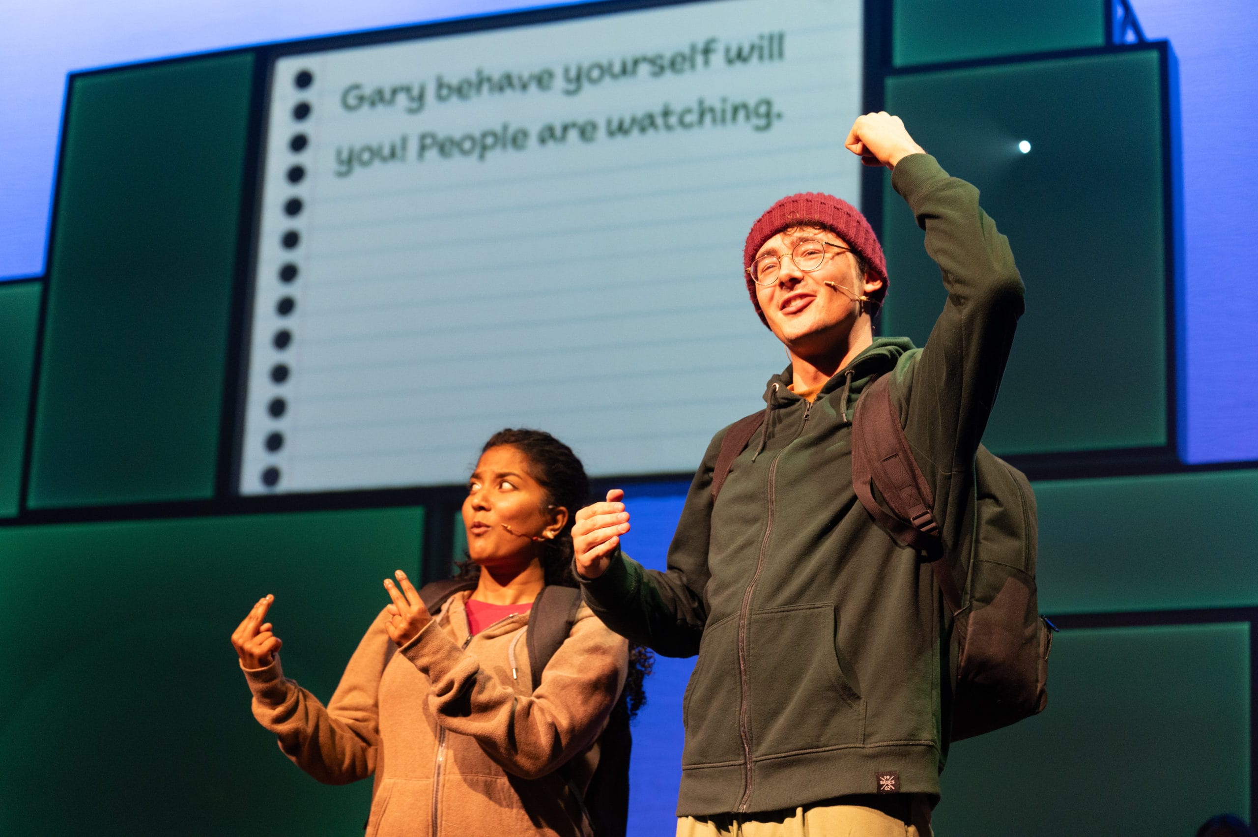 Two performers onstage. On has his hands in the air, the other is signing what he is saying.