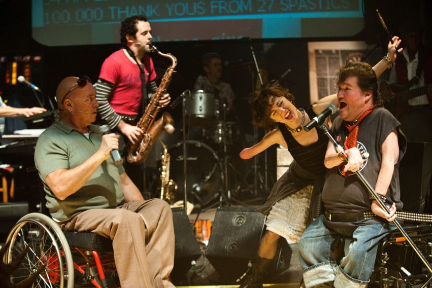A group of performers sing and play musical instruments on stage.