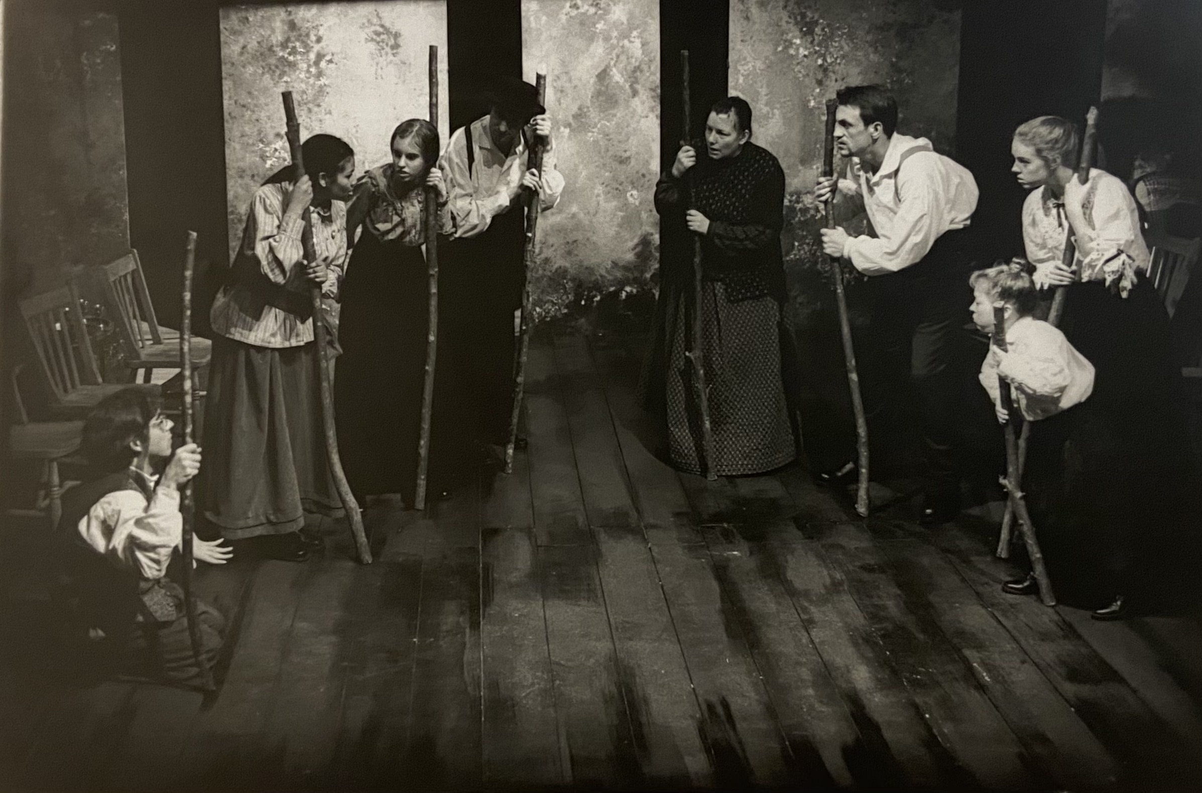 A black and white image of a group of performers standing in a circle holding large wooden stalfs.