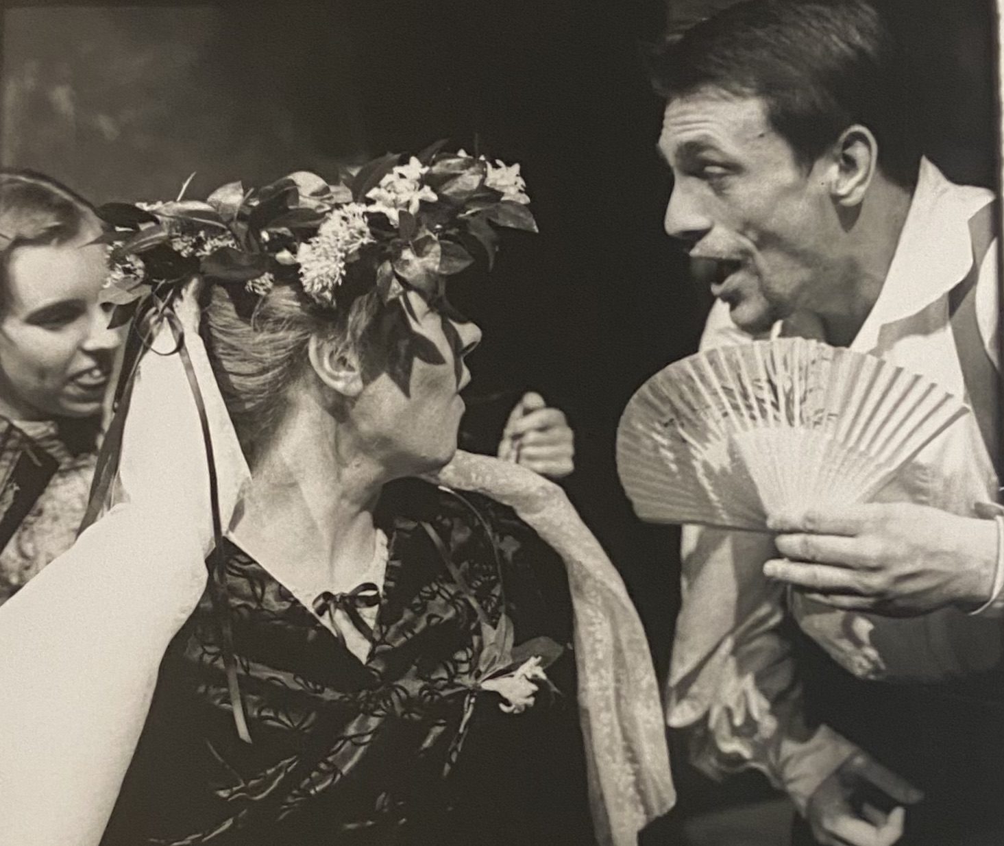 Black and white image of two performers. One holds a fan and the other has a floral headdress on. they are both looking at each other.