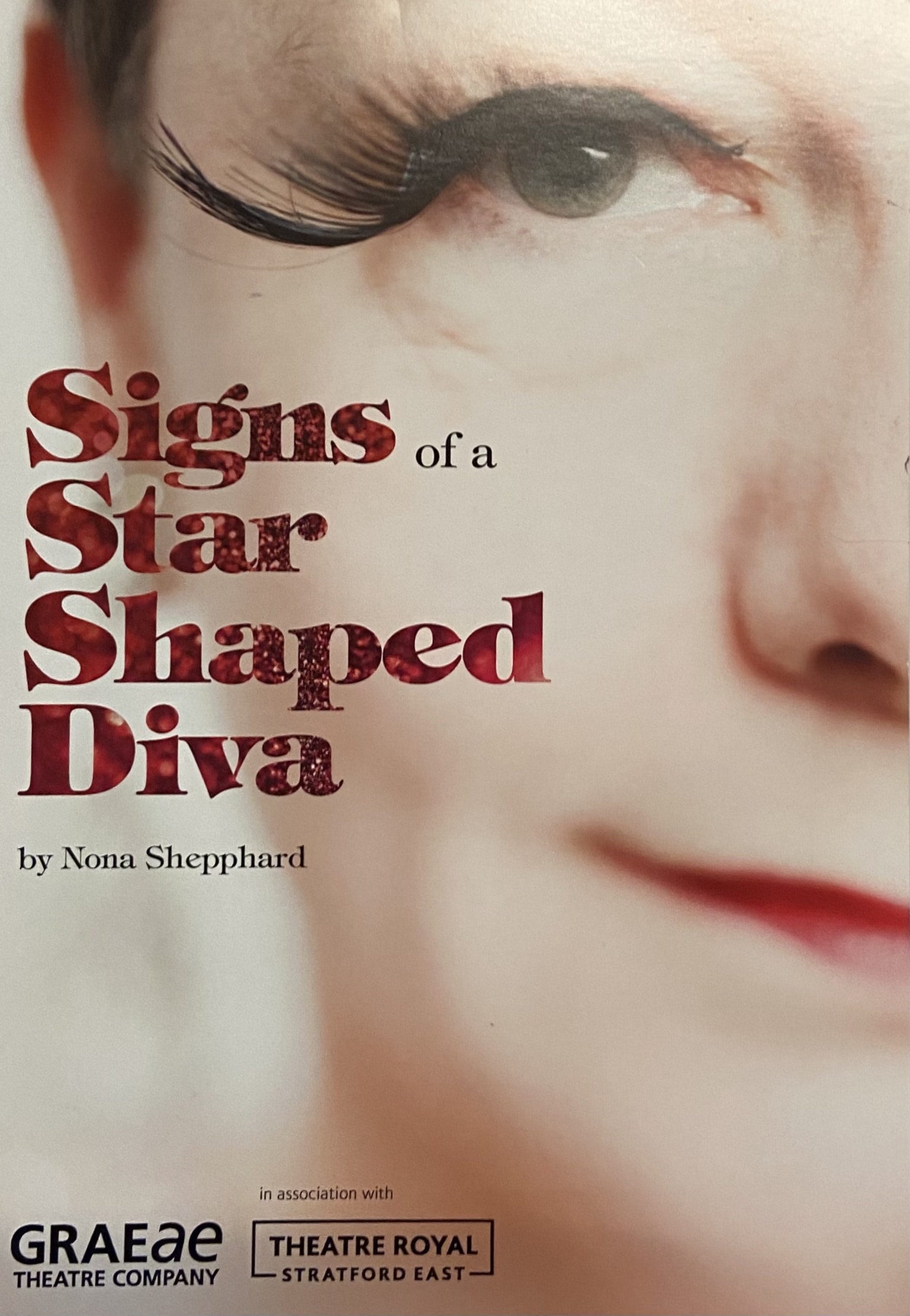 Poster for Graeae's production of 'Signs of a Star Shaped Diva', by Nona Shepphard. The poster is a close up of a white woman's face, wearing red lipstick, black eyeliner and a large false lash. The title of the play is written in red sparkly font.