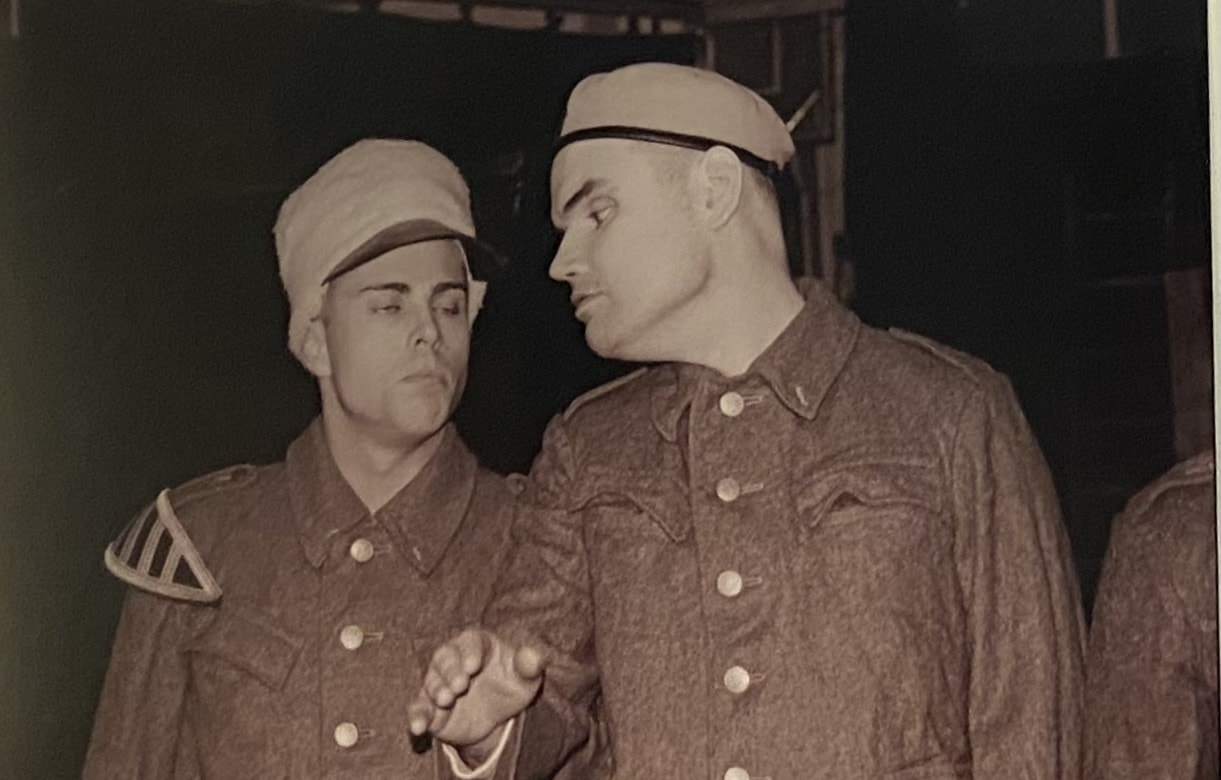 Two men dressed in army uniforms confer with each other.