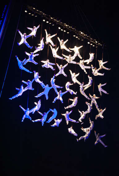 A large number of people in white suits suspended from the ceiling by ropes.