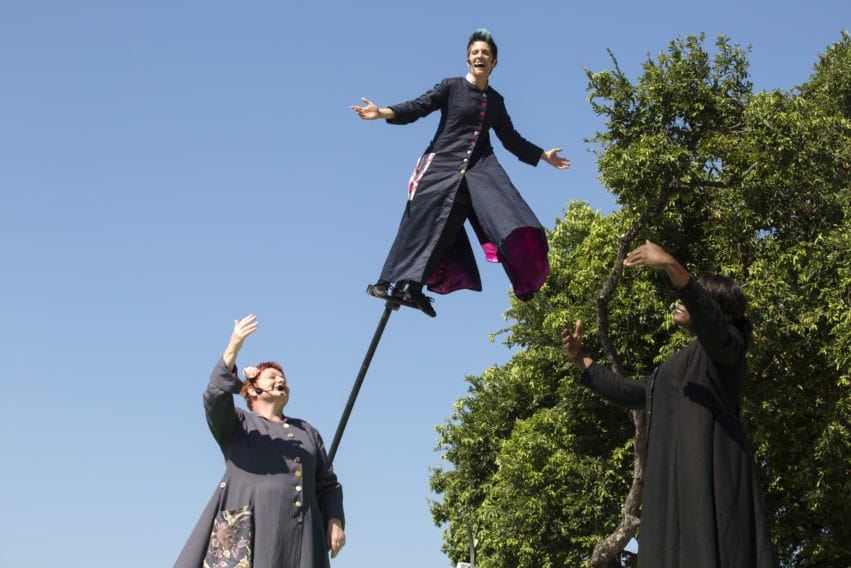 Three performers outside. One is balancing on a moving platform, the other two are on the ground.