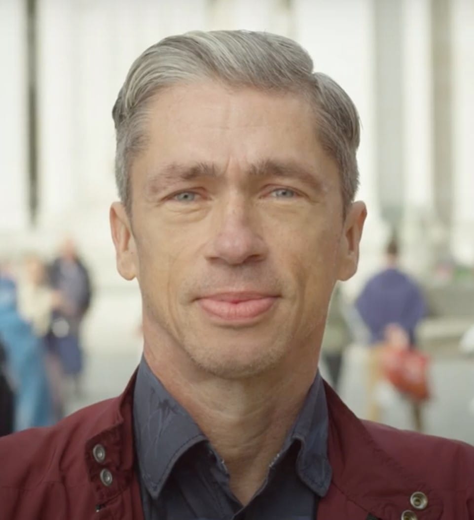 Colour headshot of Mat Fraser, he is wearing a red jacket and a blue shirt.
