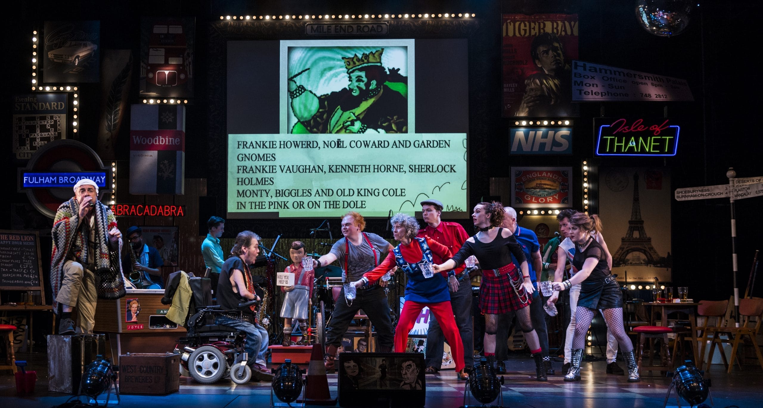 A group of performers dancing and singing. There are many signs behind them.