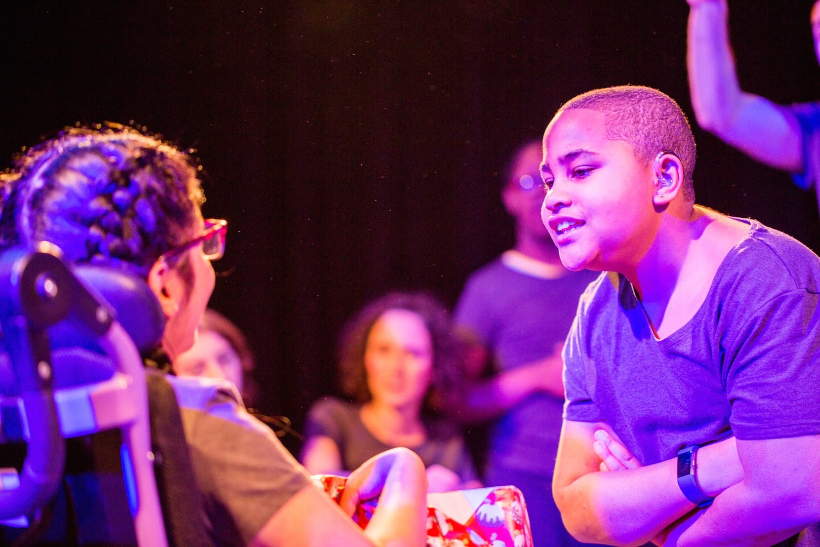Two Graeae Young Company members talking under a purple lit stage