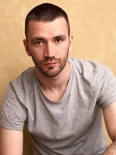 A white man with short brown hair and stubble.