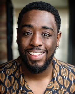 A man of colour, with short hair and some facial hair.