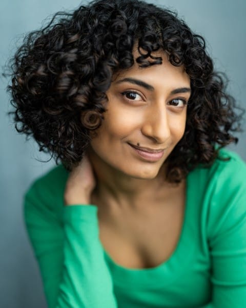 A woman of colour with short curly hair. She wears a green long sleeved top