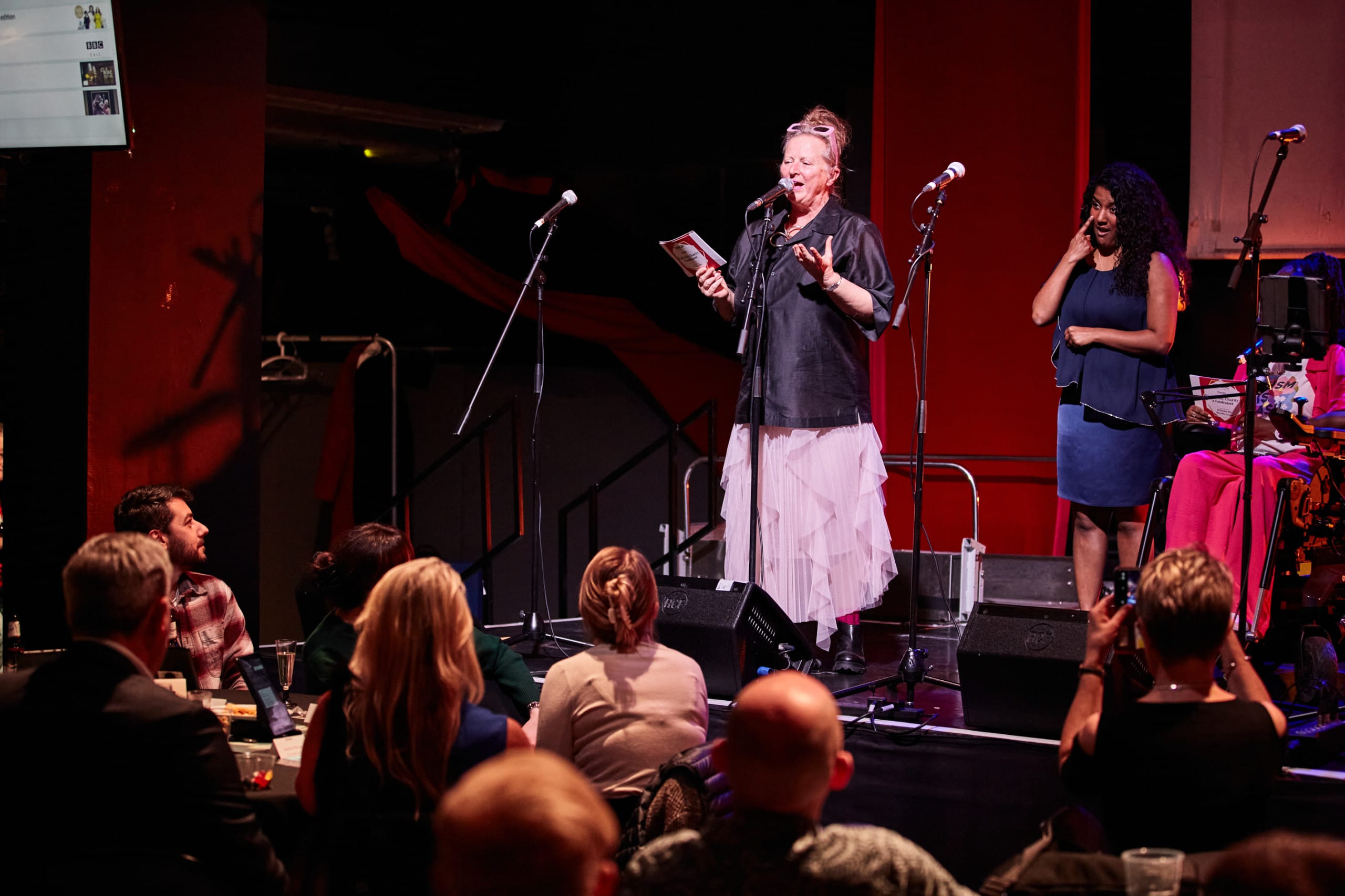 Jenny and Chandu are onstage. The audience is also in the frame.