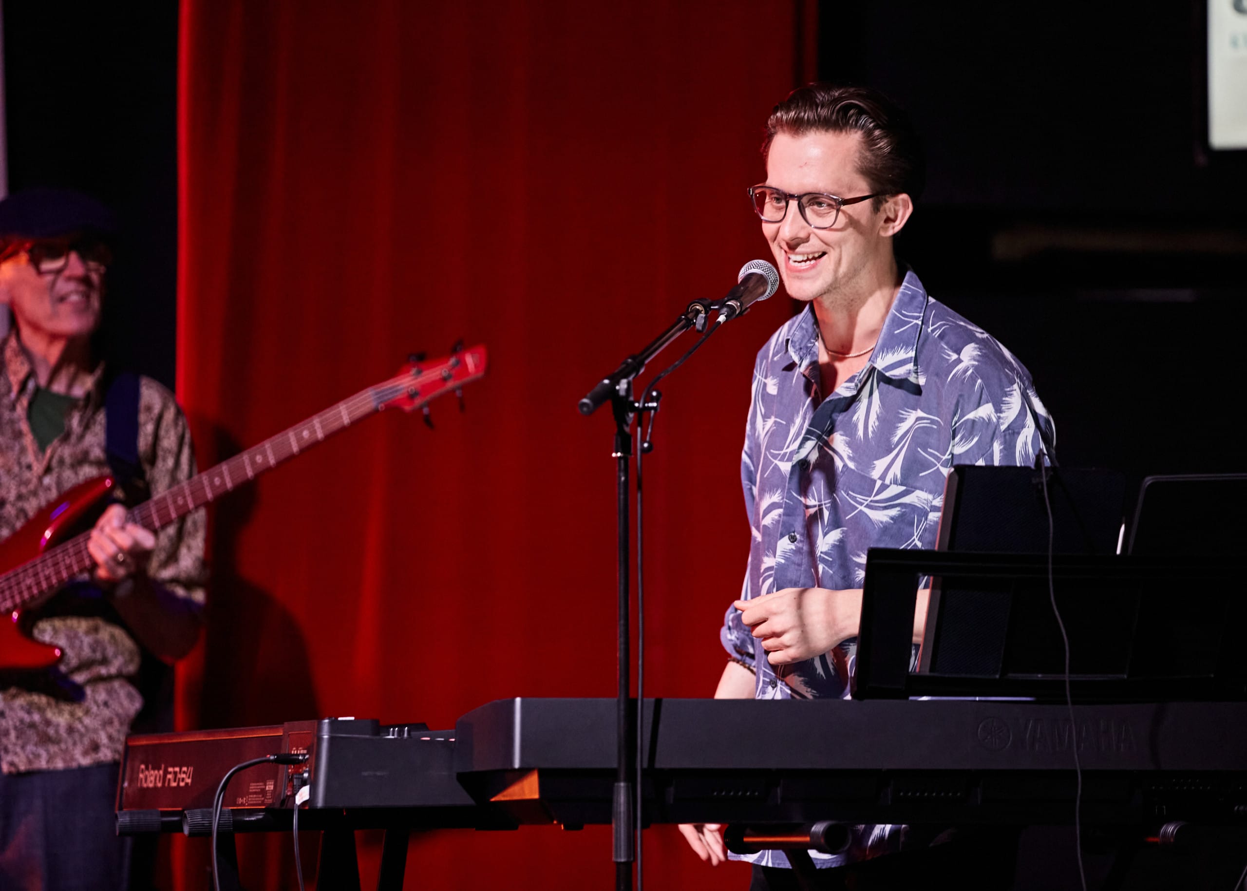 Joey, a white man wearing a blue button down and glasses, is playing the piano and singing.