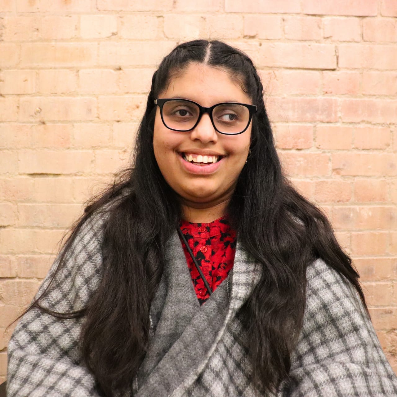 Early 20s, with long black hair that comes down, wearing glasses, and a checkered shall.