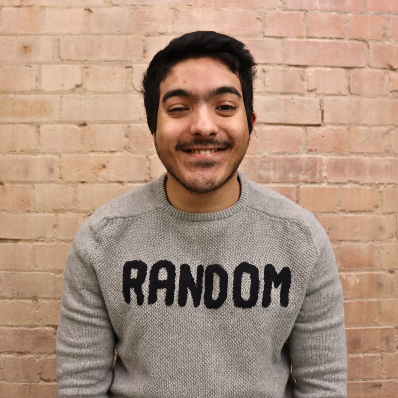 In his early 20's, wearing 2 rings, a grey random jumper, black short hair, a hearing aid,