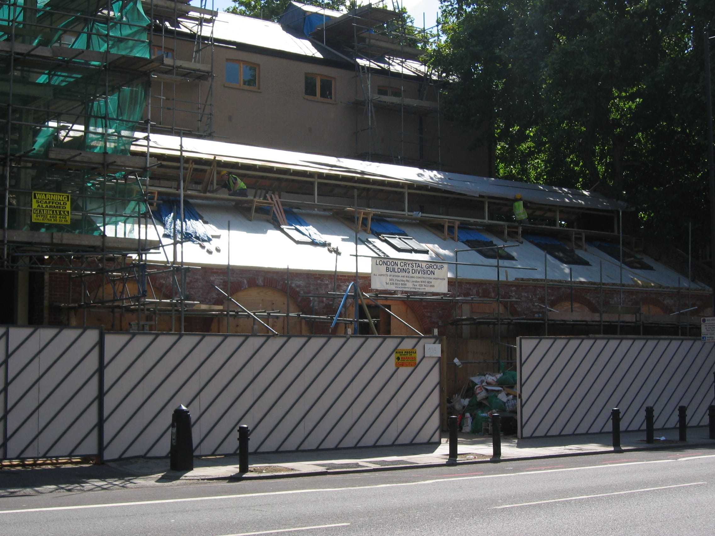 Outside of a multi-level building, there is some scaffolding and temporary walls around the outside of the building, it is under construction.