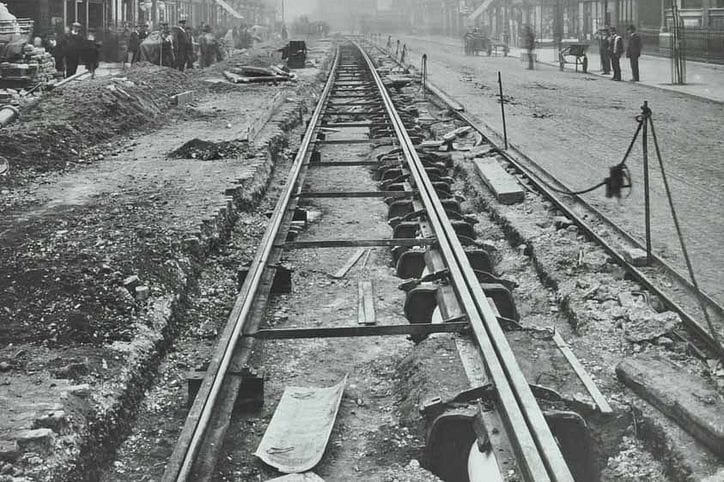 Black and white image of trainlines being laid in the middle of the road.