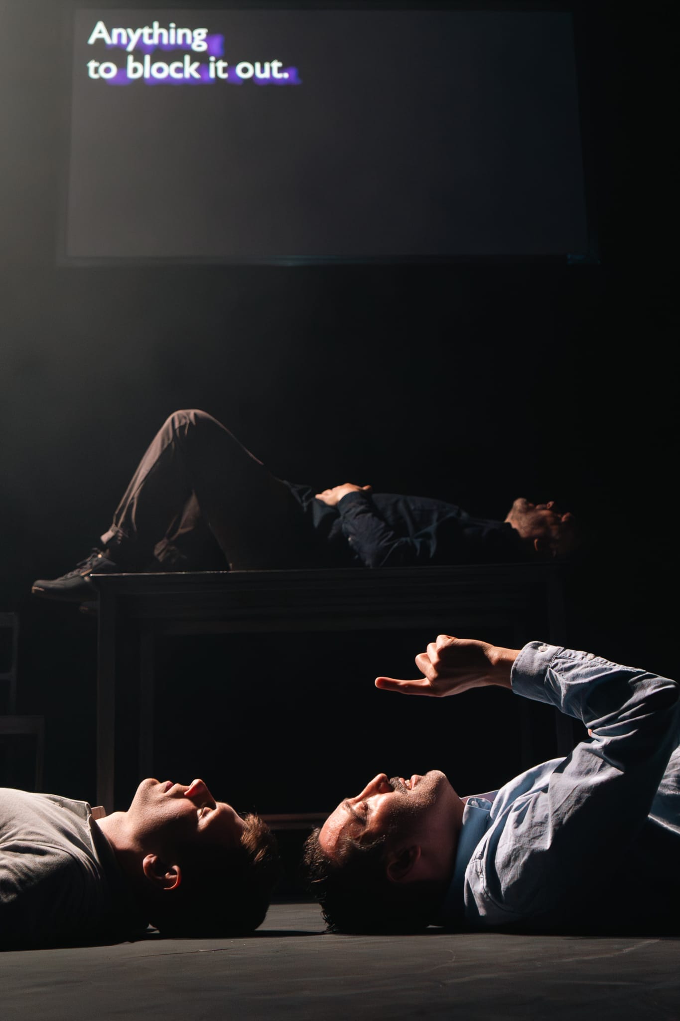 All cast members lay down, two on the floor and one behind on a table. They look up to the ceiling. Caption screen above reads, Anything to block it out.