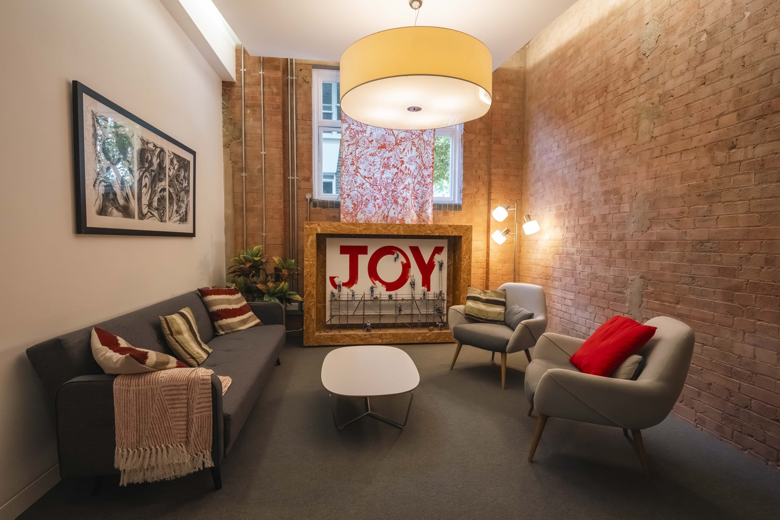 Room with soft lighting with chairs and sofas with a white table in the middle. A large Joy Sign sits in the background