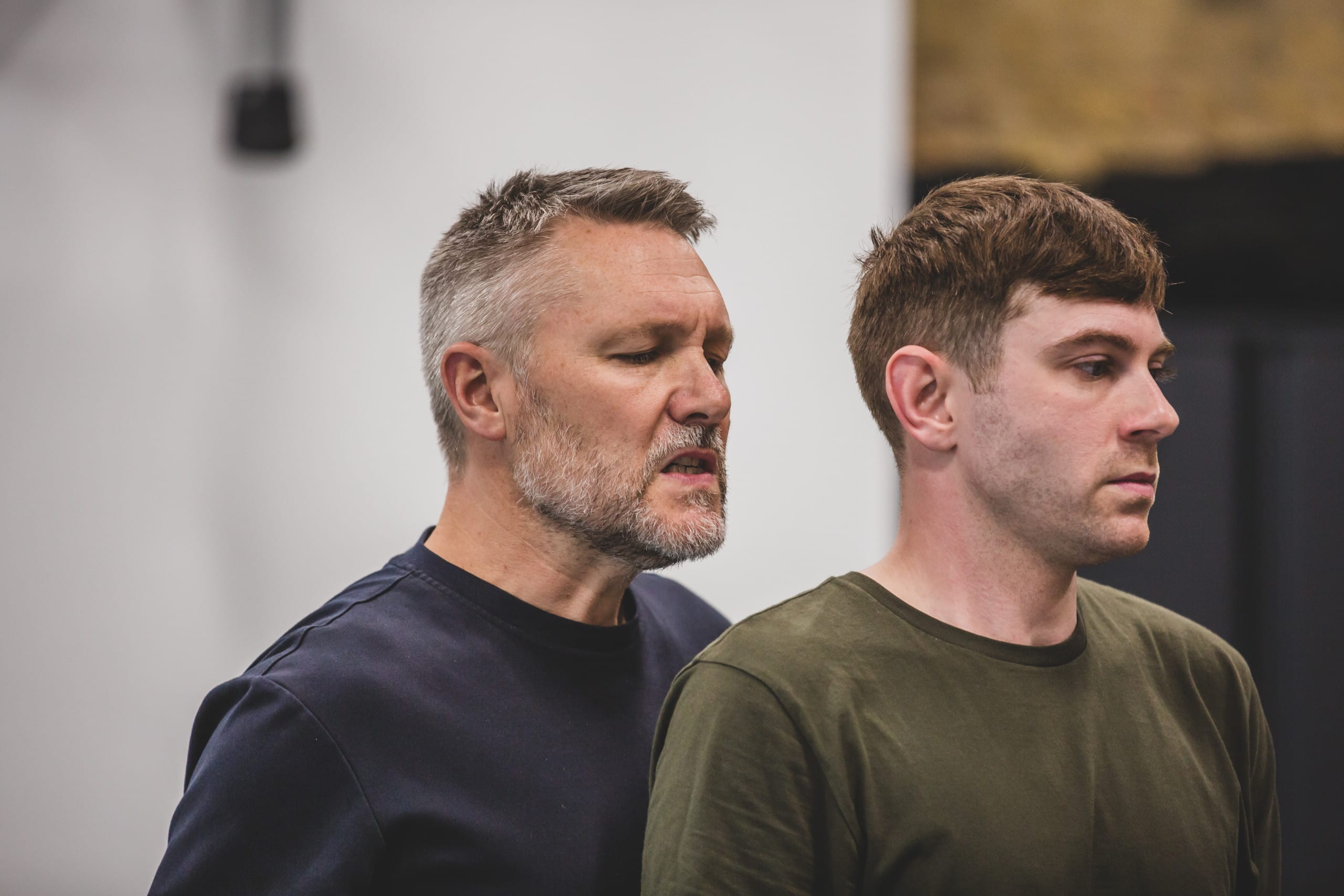 Cast member Danny Raynor stands behind other cast member Robin Paley Yorke with an intense look on his face while Robin looks on nervously.