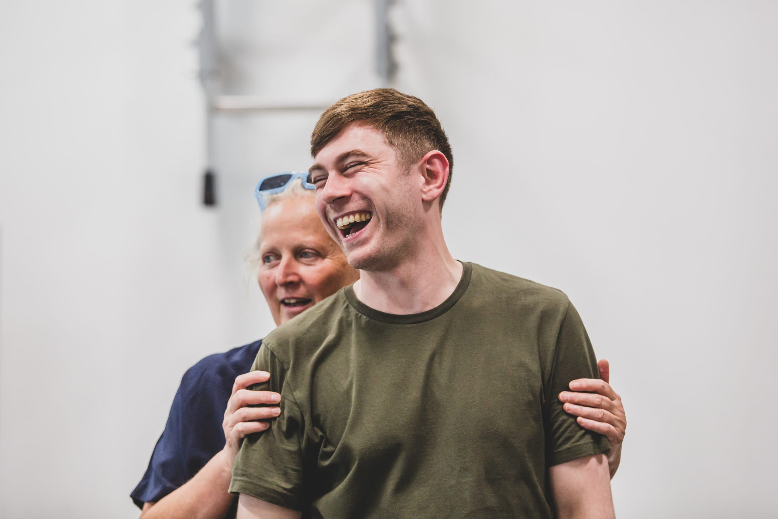 Director Jenny Sealey stands behind cast member Robin Paley Yorke holding his arms while they both smile and laugh.