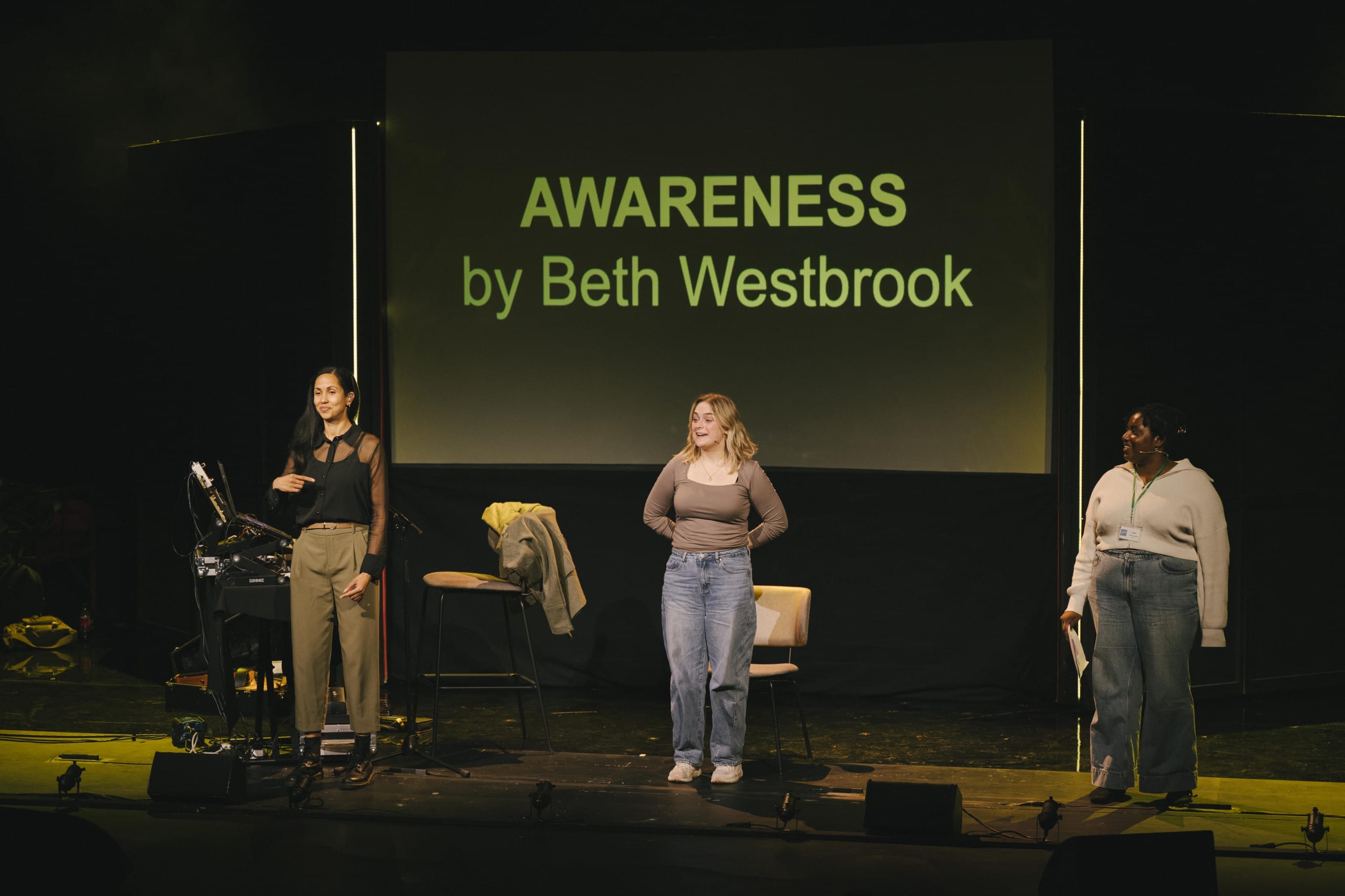 Three people standing beside each other on stage with a caption board in the background.