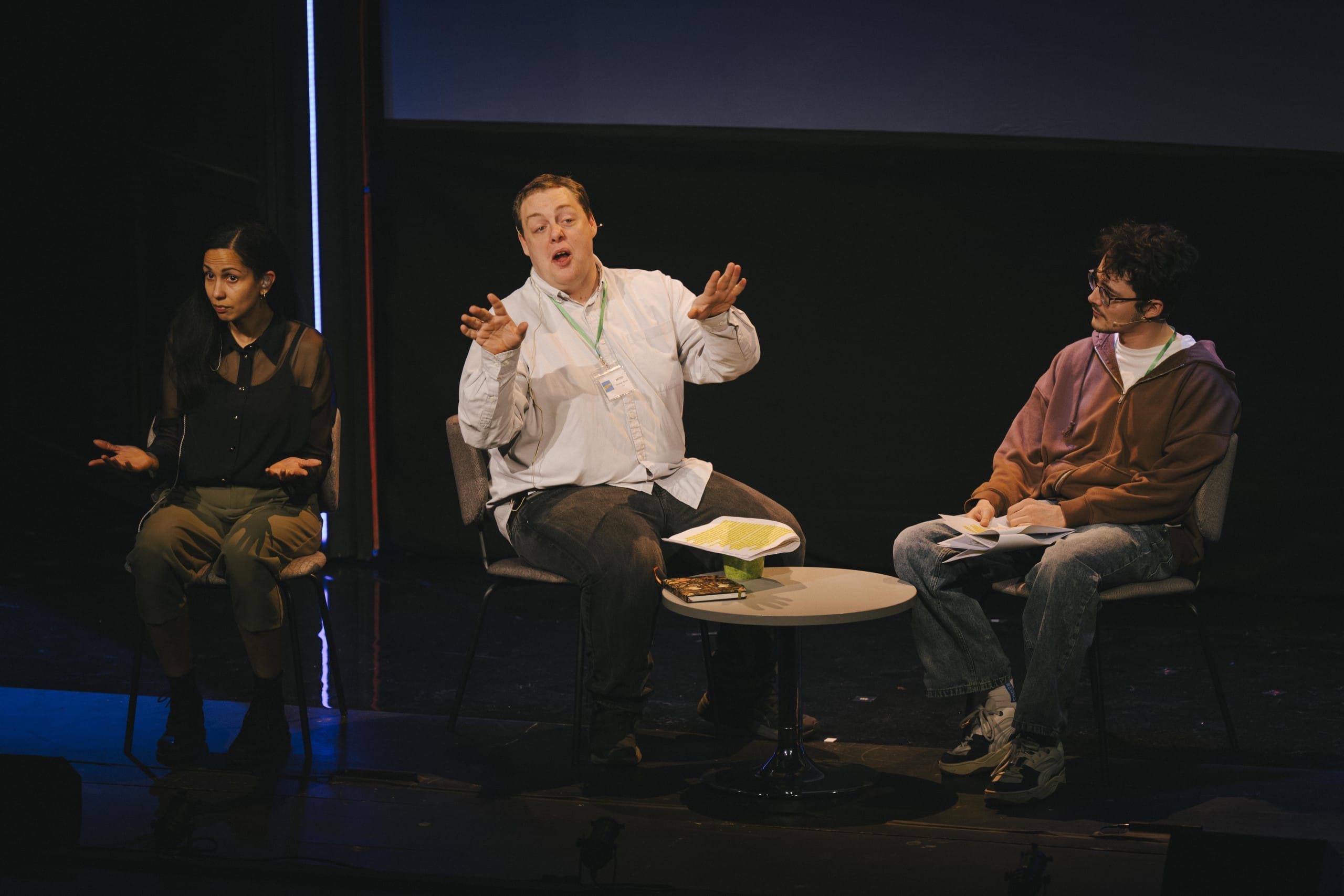 Two people on stage sitting down performing a rehearsed reading. An interprter is to the side.